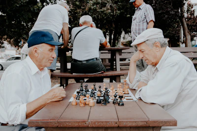 Two friends smiling and playing chess on a tablet in a park.