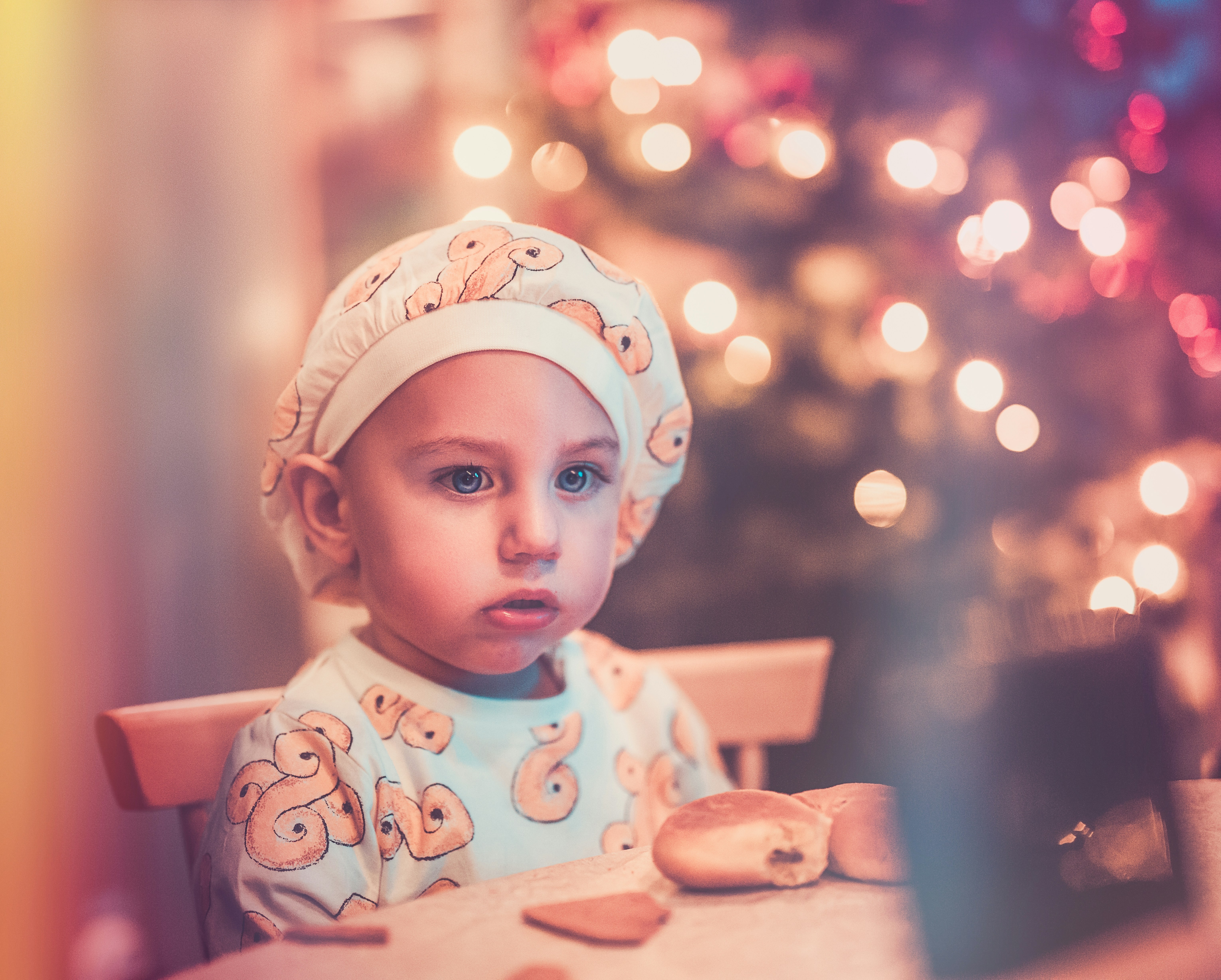 baby sitting next to a table with bread