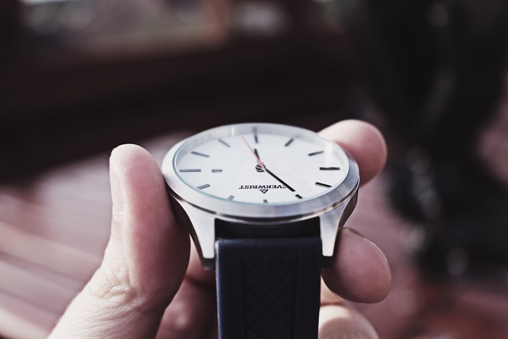 person holding silver-colored analog awtch with black strap