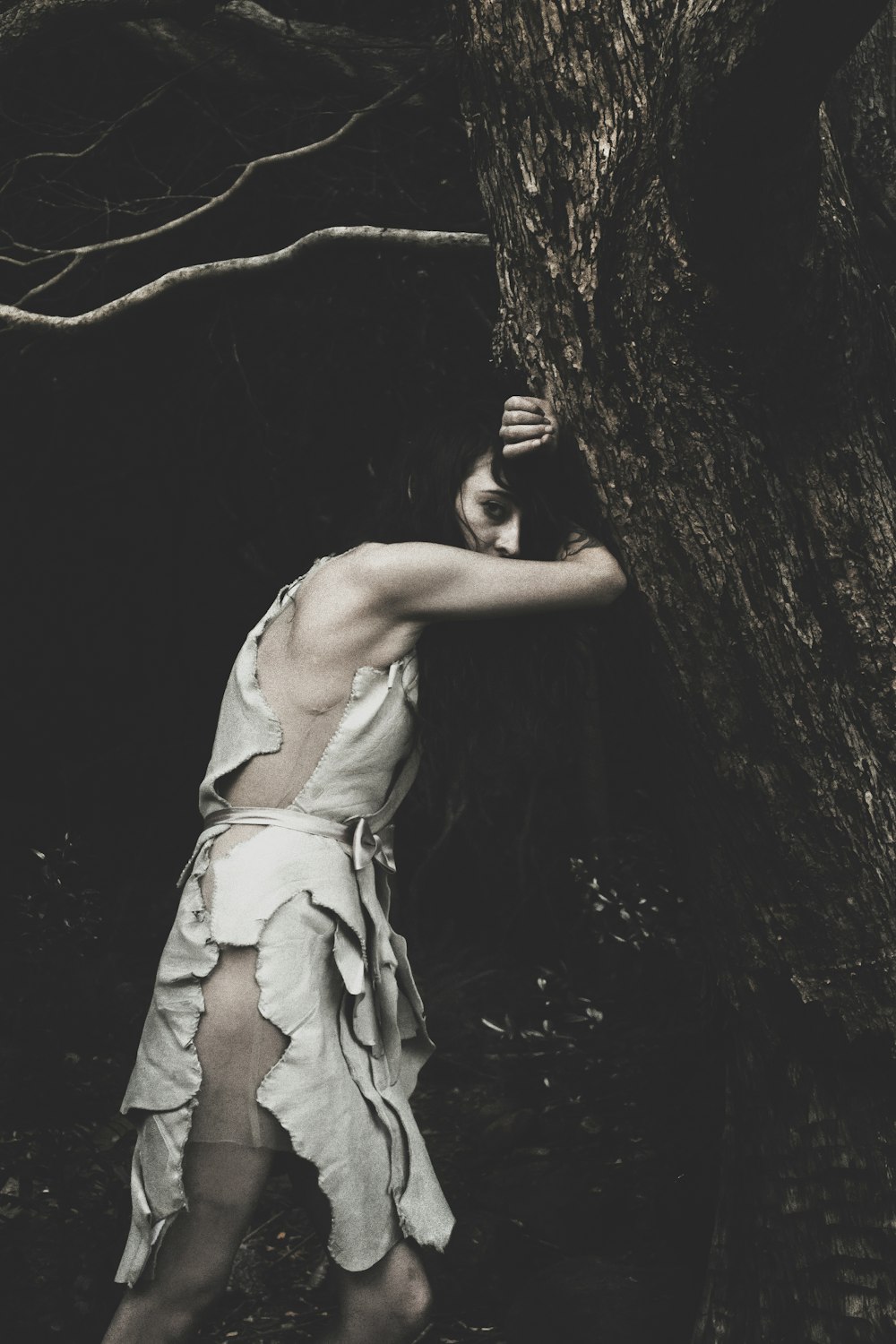 black haired woman leaning on tree trunk