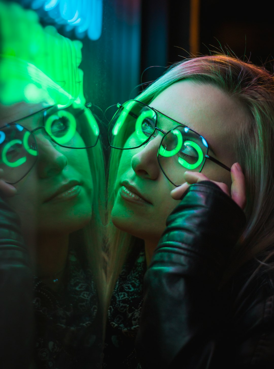 woman facing mirror with green and blue neon signage