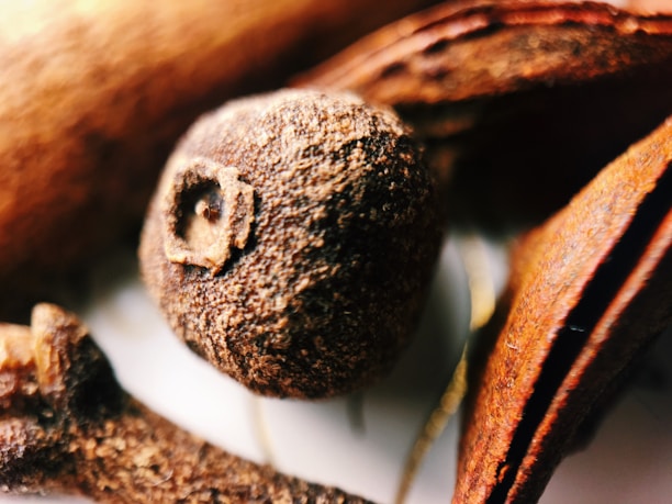 Close-up of dried clove buds spilling from a rustic wooden bowl.