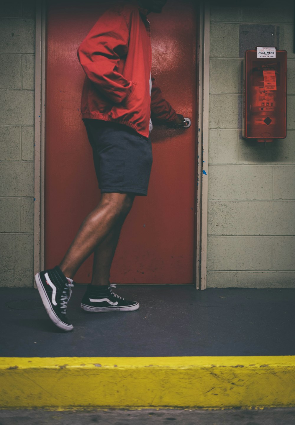 man wearing red jacket holding door knob near red wooden door