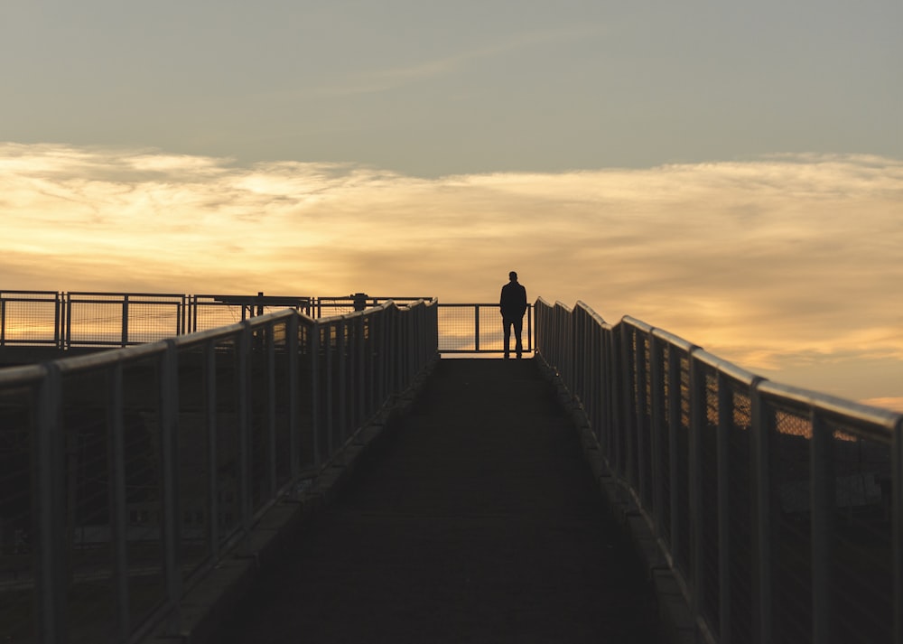 silhouette fotografia dell'uomo in piedi sull'angolo del ponte