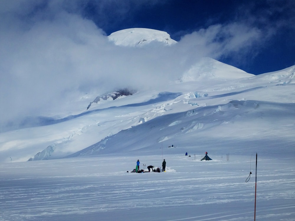 group of people standing on snow near tipi tent and snow covered mountain under white clouds during daytime