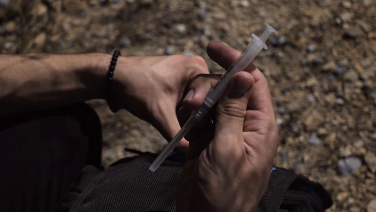 Man's hand holding a syringe, illustrating a testosterone injection and weekly dosing schedule.