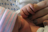 A close-up of a newborn baby’s tiny hand gripping a doctor’s finger during a vaginal delivery.