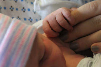 Close-up of a tiny baby's hand gripping a caregiver's finger with tender care.