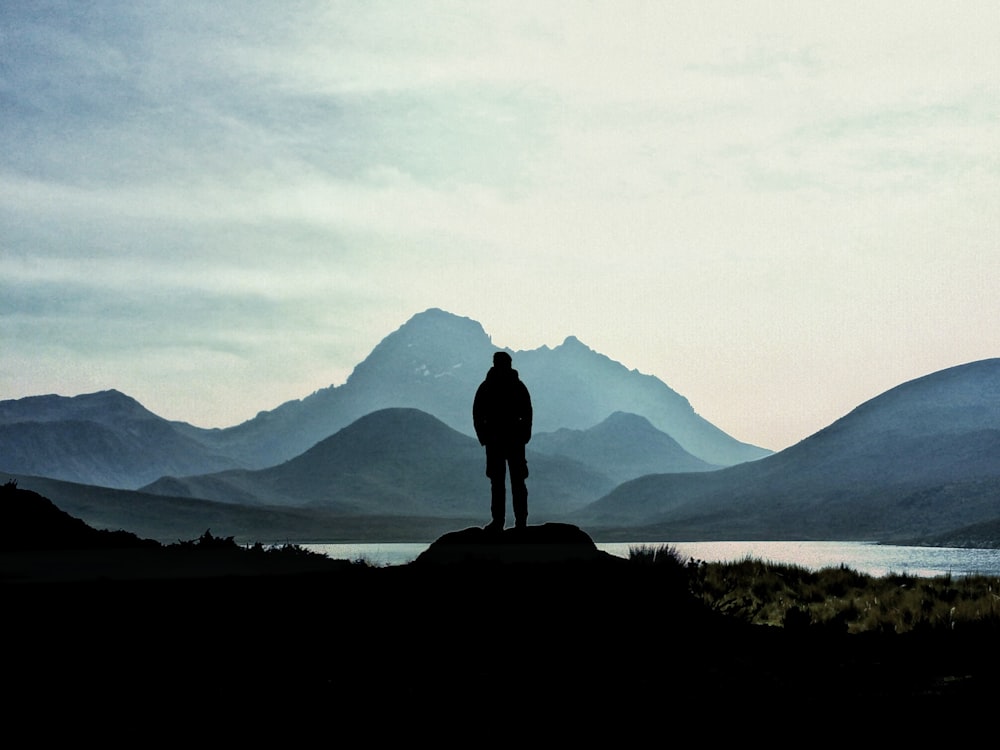 silhouette of man standing on rock near the lake