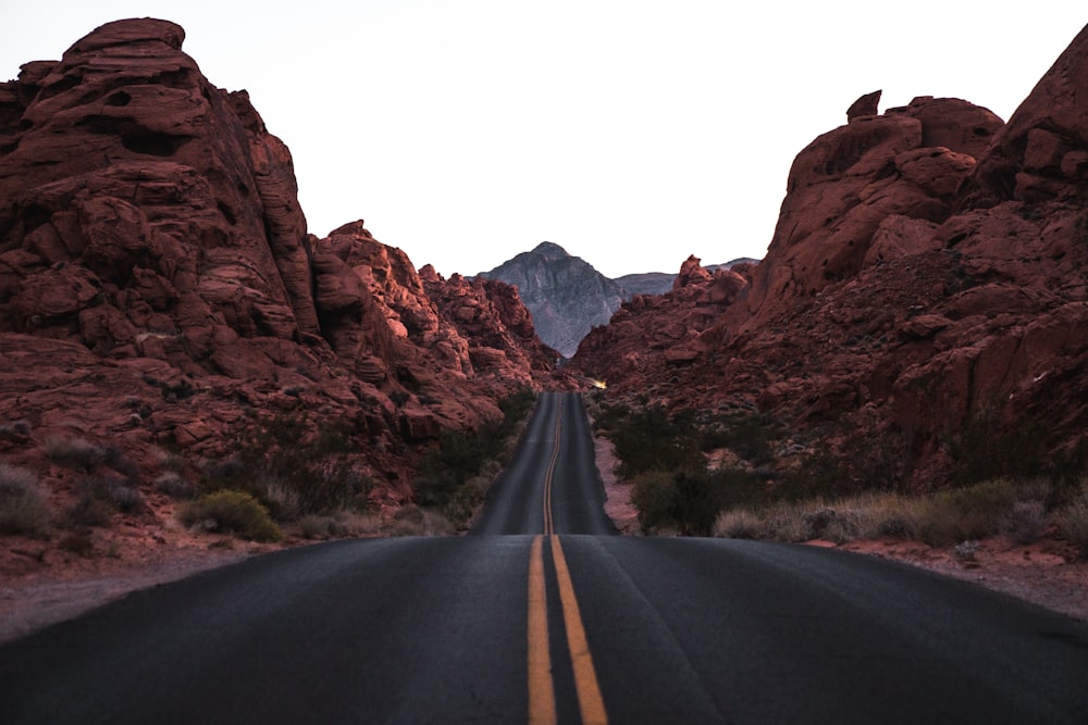 black and yellow concrete road beside brown rocky hills