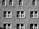 A stone building facade with symmetrical rows of windows. The walls are constructed from textured bricks, creating a repeating pattern. Each window has a white frame and is divided into smaller panes. Some windows are rectangular, while others have an arched top.