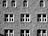 A stone building facade with symmetrical rows of windows. The walls are constructed from textured bricks, creating a repeating pattern. Each window has a white frame and is divided into smaller panes. Some windows are rectangular, while others have an arched top.