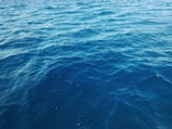 Waves of the ocean extend into the horizon, creating a rhythmic pattern of dark blue shades. The water appears calm with subtle ripples across the surface.