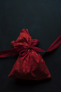 A red fabric pouch adorned with small golden heart patterns is tied with a matching red ribbon against a dark background.