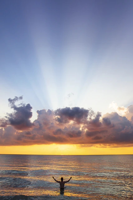 man raising his arms on sea under black clouds