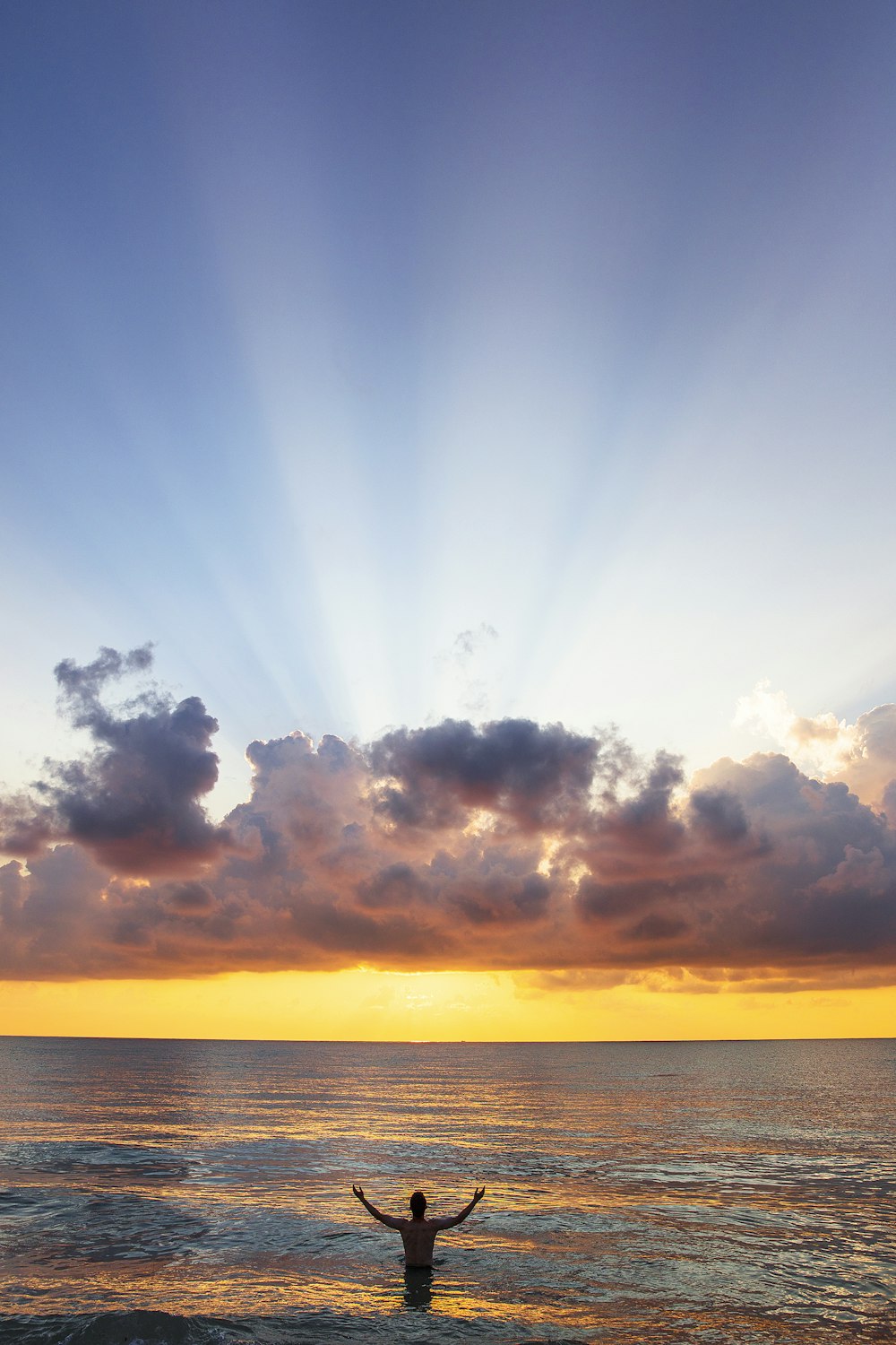 homem erguendo os braços no mar sob nuvens negras