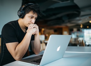 man wearing headphones while sitting on chair in front of MacBook