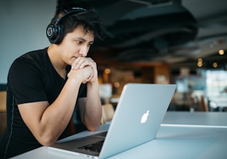 man wearing headphones while sitting on chair in front of MacBook