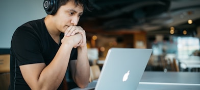 man wearing headphones while sitting on chair in front of MacBook