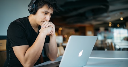 man wearing headphones while sitting on chair in front of MacBook