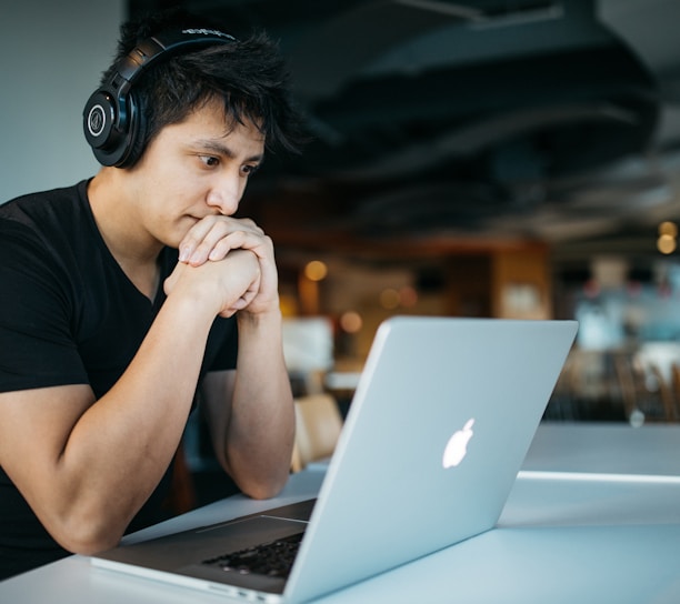 man wearing headphones while sitting on chair in front of MacBook