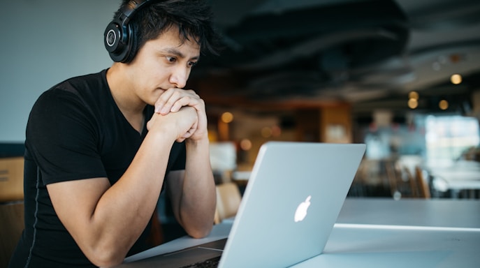 man wearing headphones while sitting on chair in front of MacBook