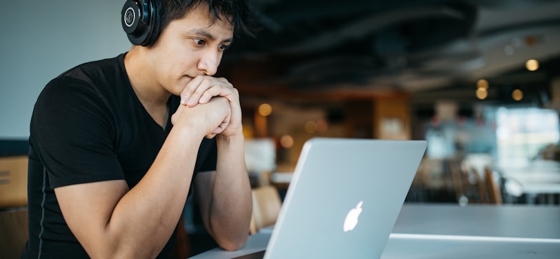 man wearing headphones while sitting on chair in front of MacBook