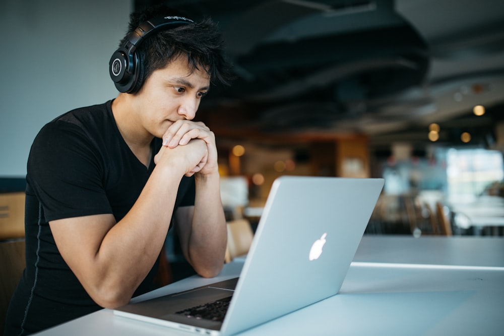 Mann mit Kopfhörern, während er auf einem Stuhl vor dem MacBook sitzt