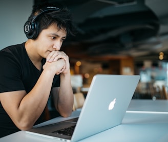 man wearing headphones while sitting on chair in front of MacBook