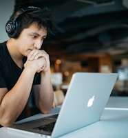 man wearing headphones while sitting on chair in front of MacBook