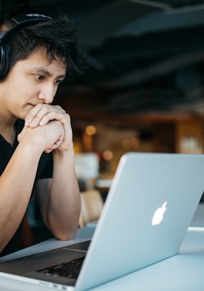 man wearing headphones while sitting on chair in front of MacBook