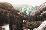 A hiker standing on a ridge overlooking a vast valley filled with pine trees