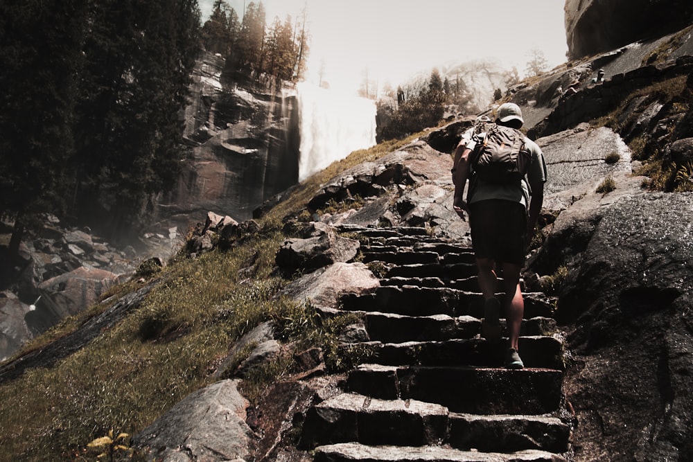 man walking up stone stairs near a waterfall at daytime