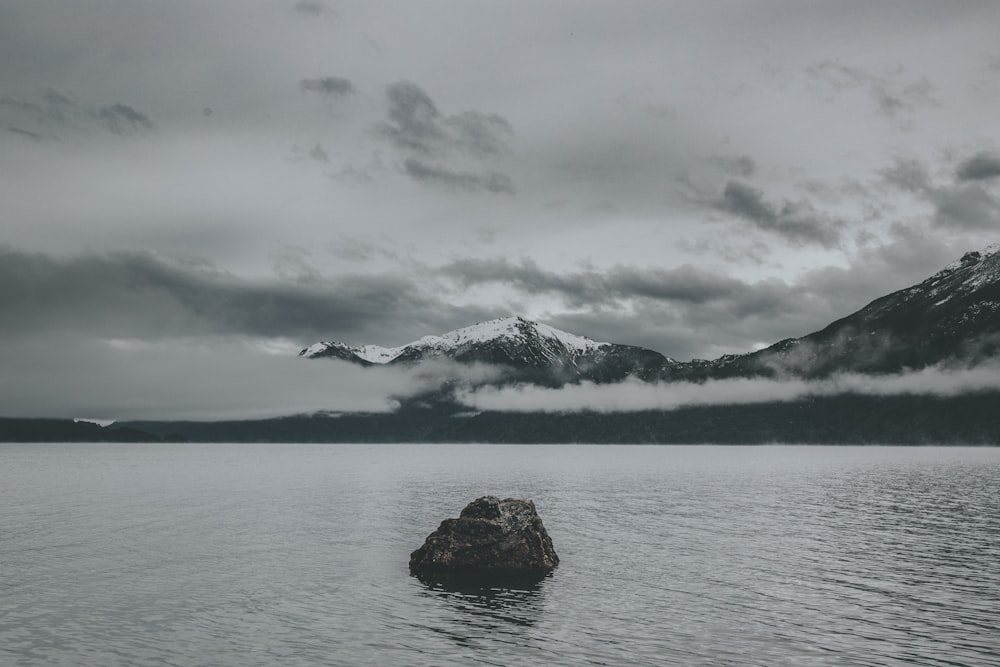 body of water near mountain under the cloudy sky
