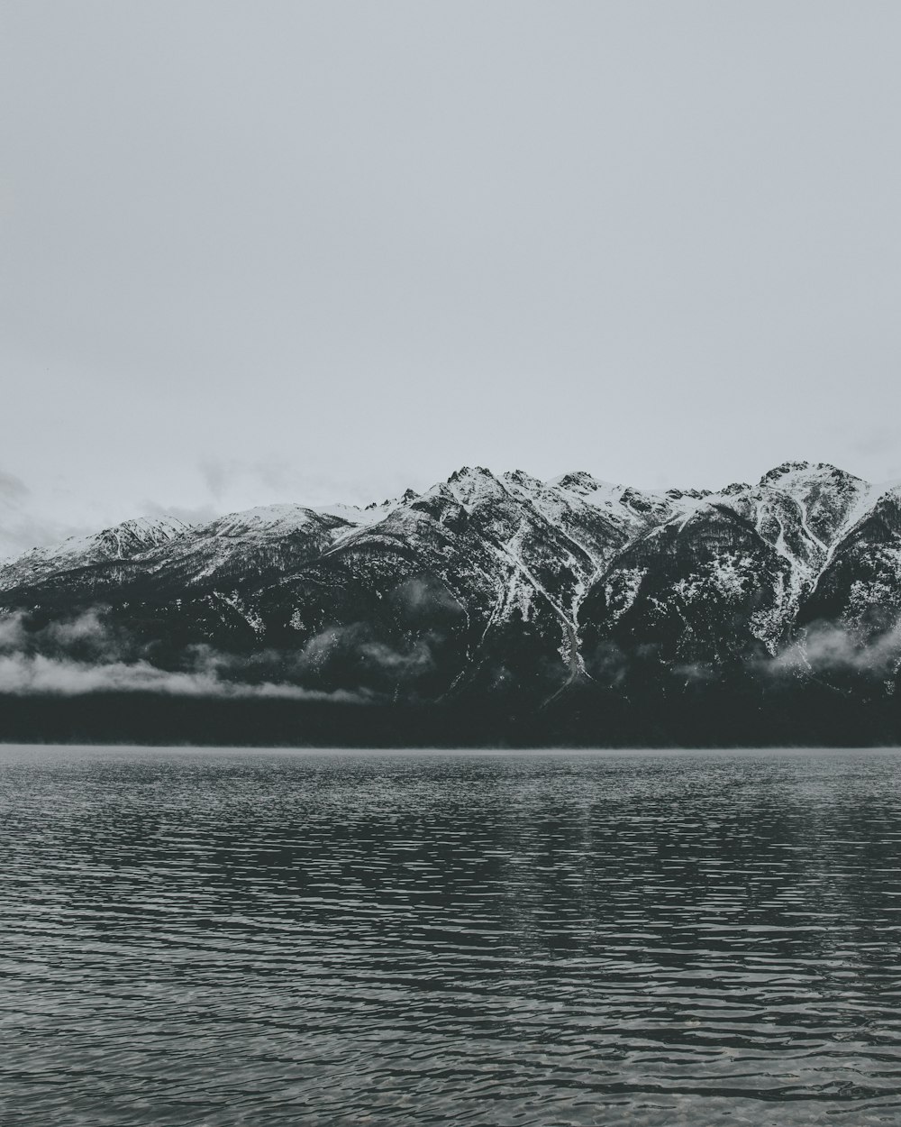 Graustufenfoto eines Berges in der Nähe eines Gewässers