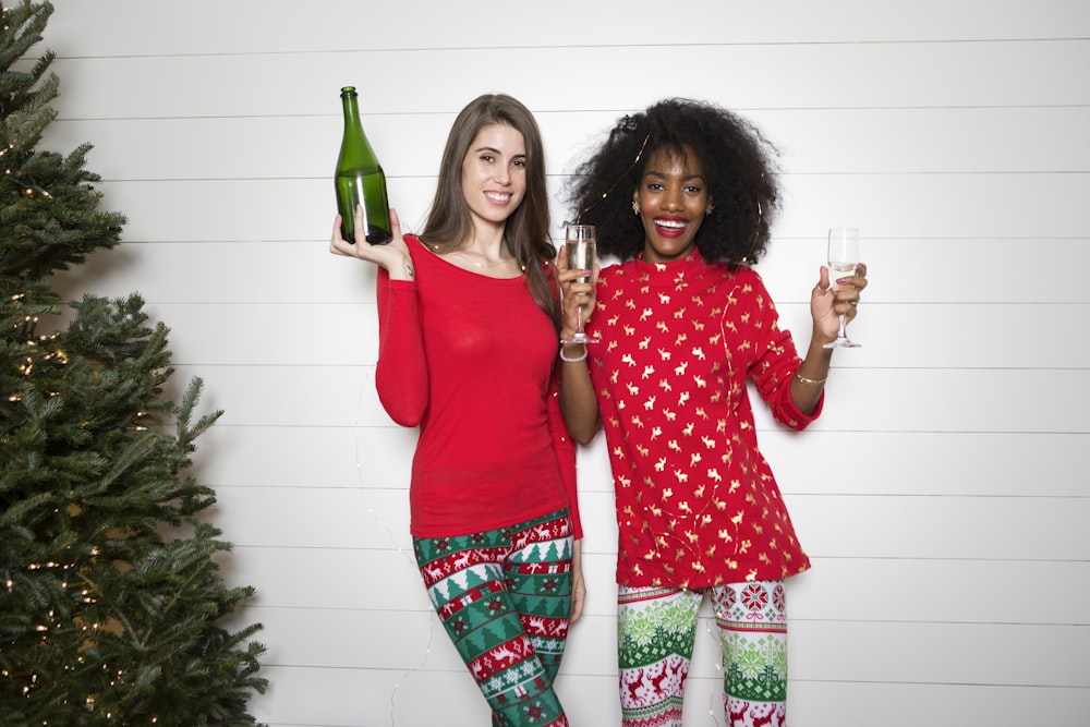 mujer sosteniendo botella de vino mientras otra mujer sosteniendo dos copas de vino transparentes
