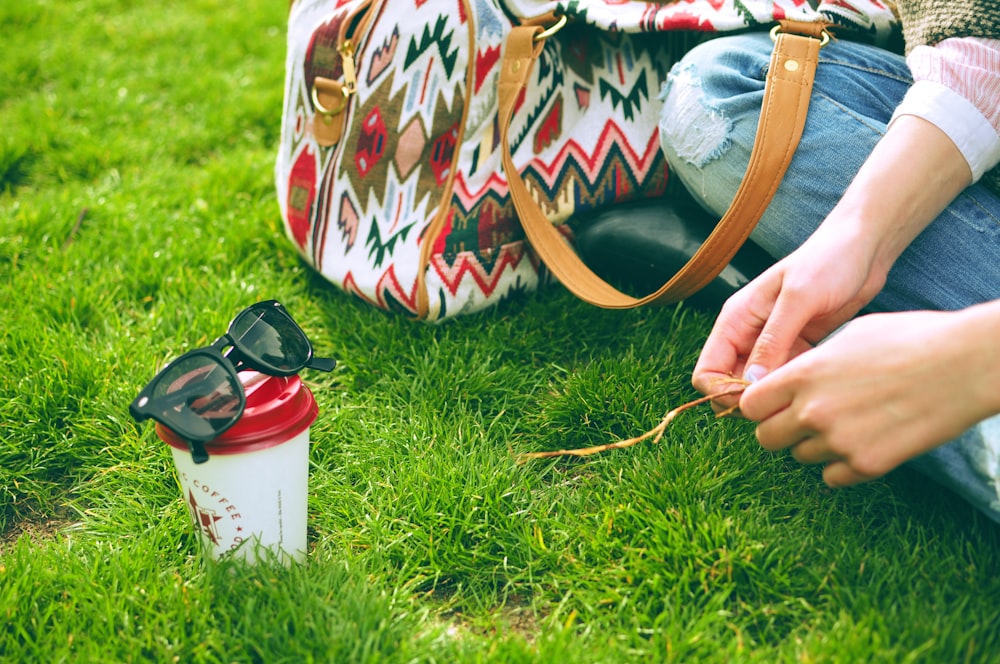 person sitting on grass near bag and cup at daytime