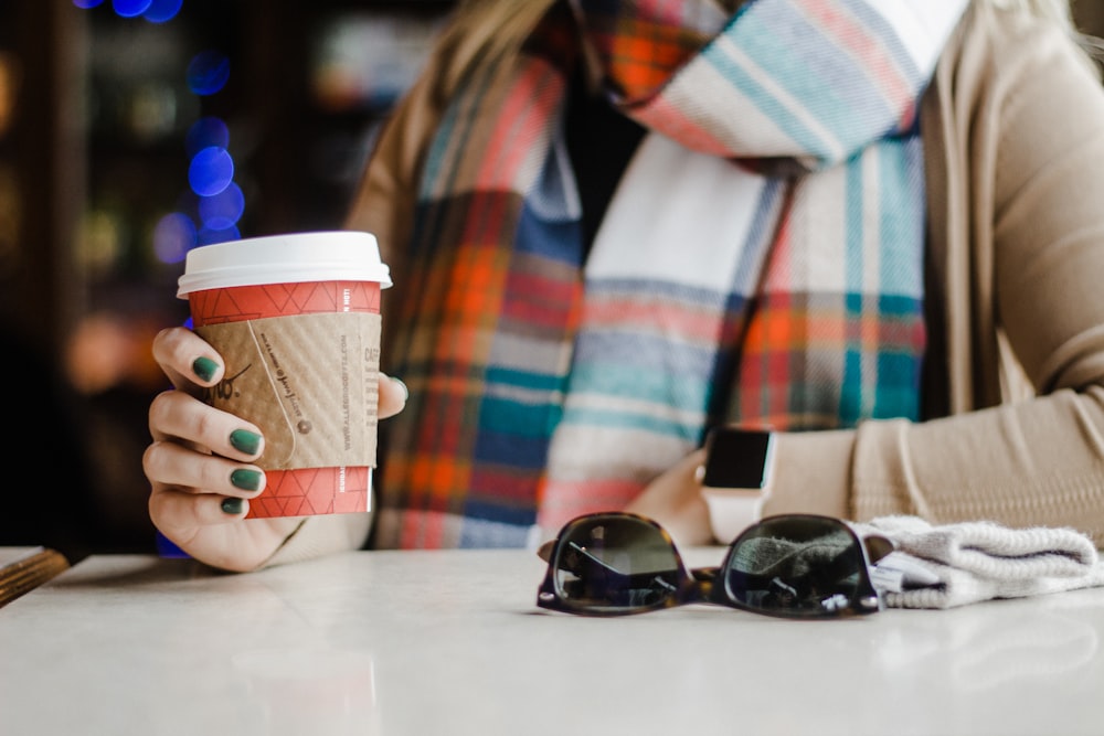 woman holding white disposable cup while leaning on table