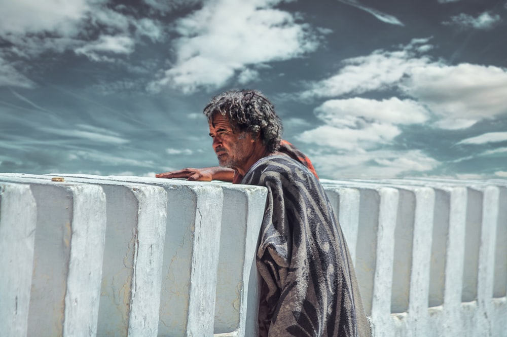 person with black hair leaning on concrete wall under white clouds during daytime