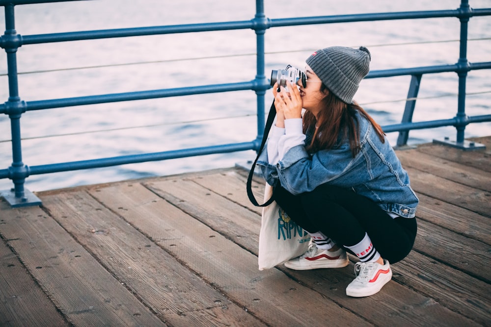 woman sitting on brown boardwalk holding DSLR camera taking photo