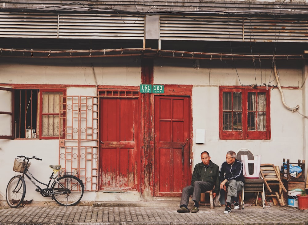 two men sits beside brown wooden door during daytime