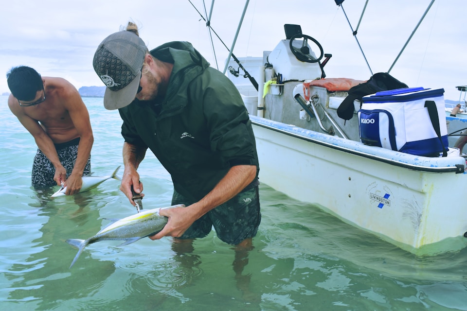 Two men gutting fish in front of a small boat.