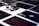 A stack of poker chips with a distinctive black and white pattern is placed on a table covered with several playing cards. The cards are dark with red and white symbols, creating a bold contrast against the lighter surface.