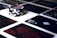 A stack of poker chips with a distinctive black and white pattern is placed on a table covered with several playing cards. The cards are dark with red and white symbols, creating a bold contrast against the lighter surface.
