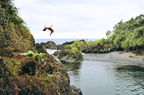 man back tumbling on gray rock formation near sea during daytime