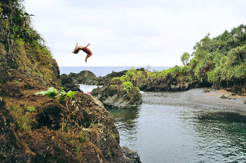 man back tumbling on gray rock formation near sea during daytime