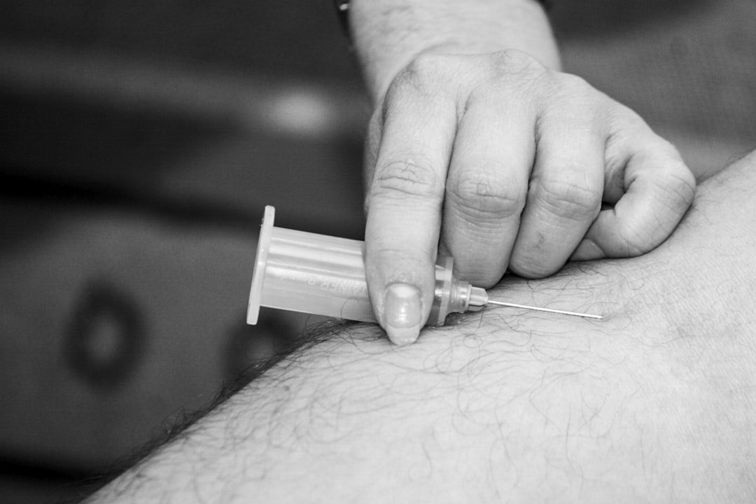 grayscale photo of person holding syringe, A person about to give blood