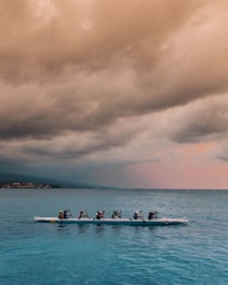 people on white and blue boat paddling under gray clouds during daytime