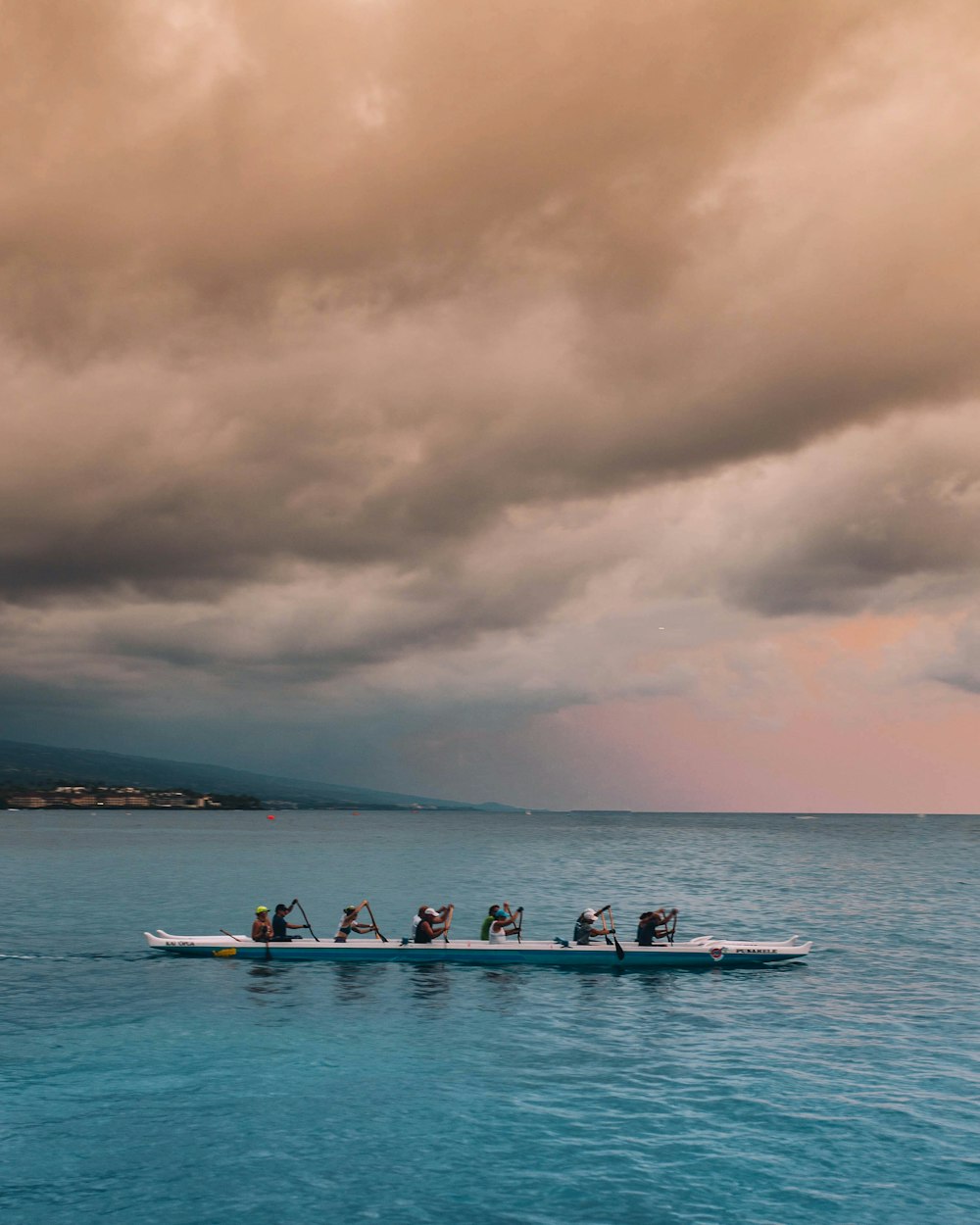 personnes sur un bateau blanc et bleu pagayant sous des nuages gris pendant la journée