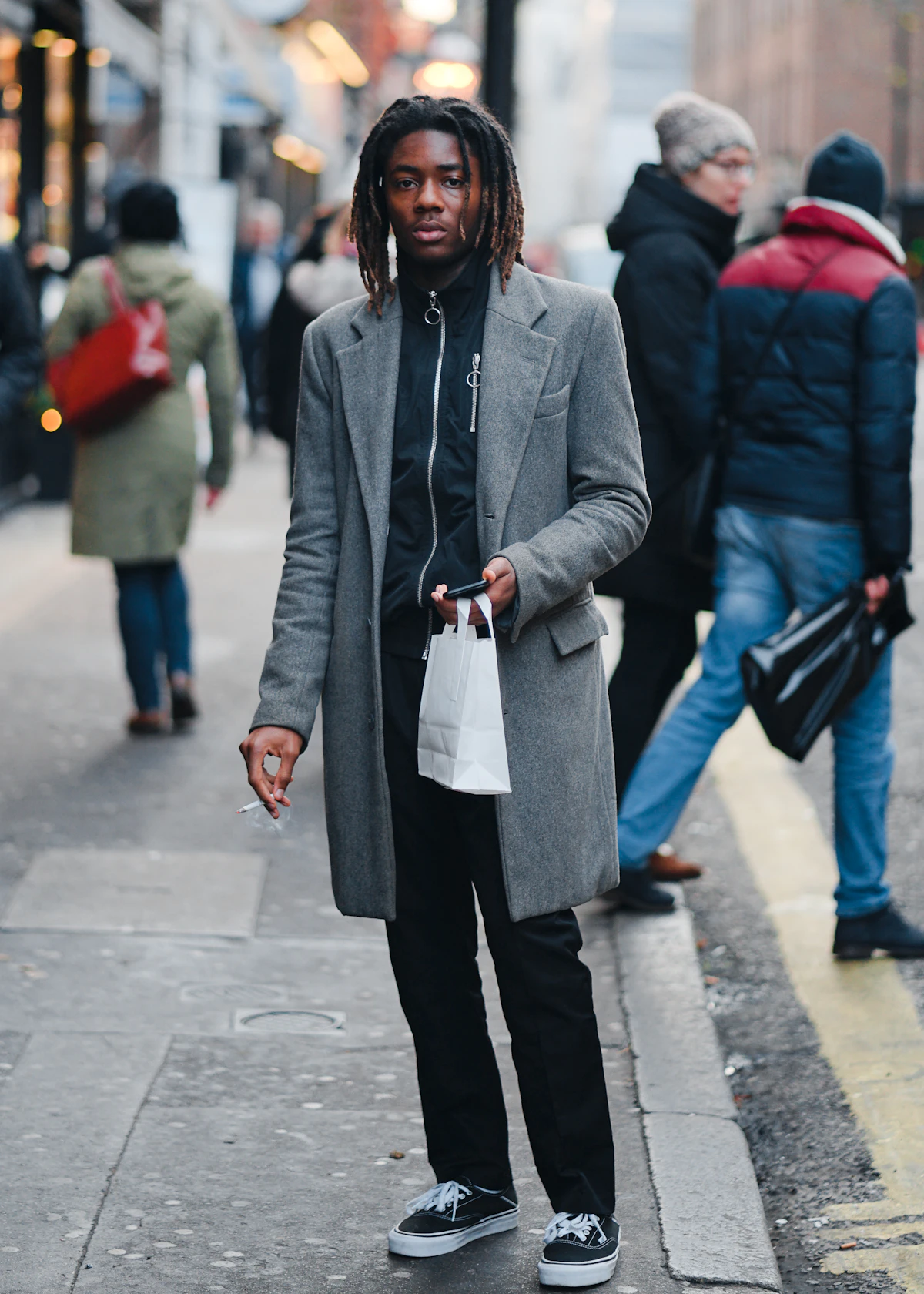 Man in grey overcoat walking with shopping bags on autumn city sidewalk